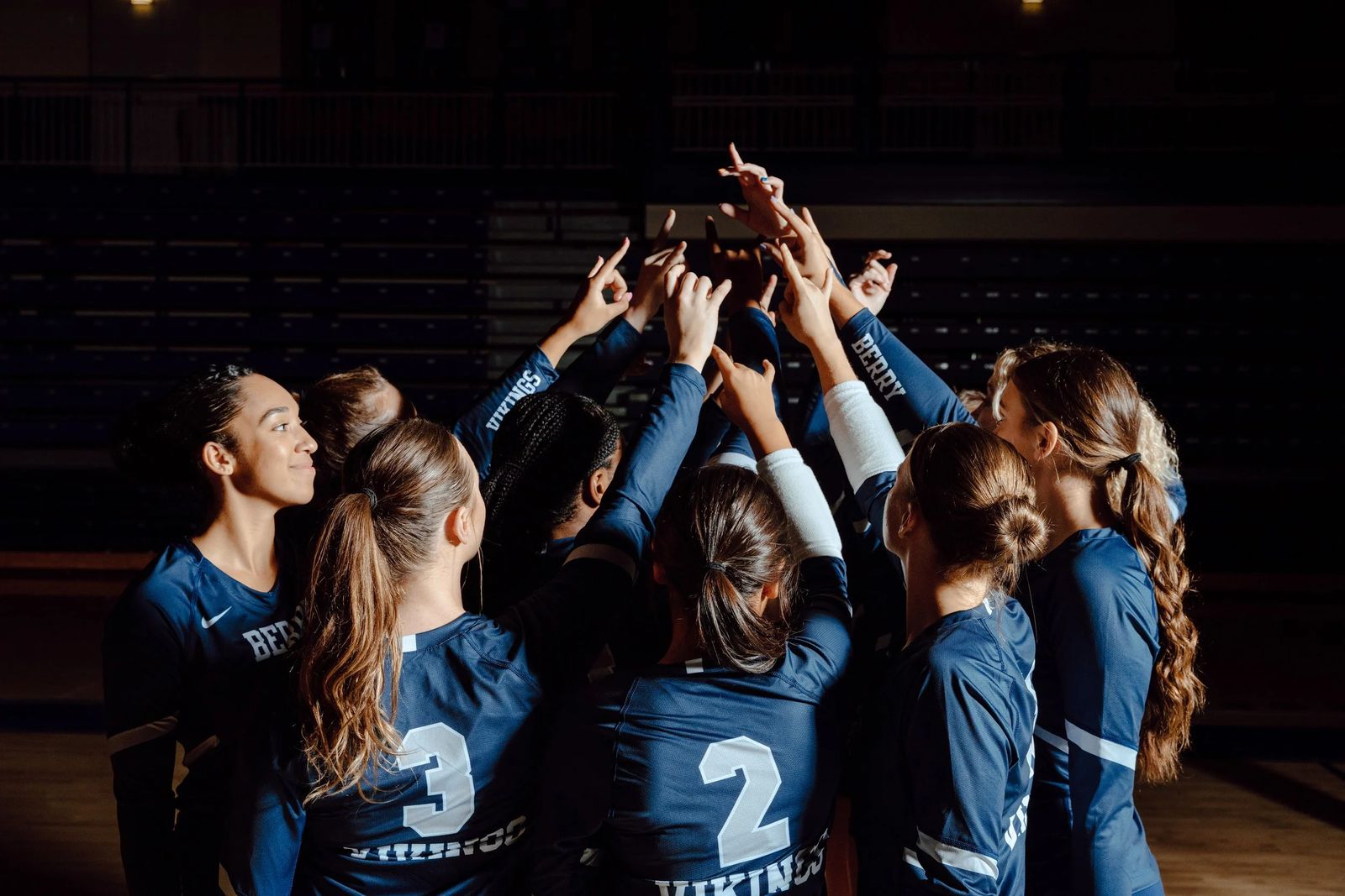A volleyball team huddled around a championship trophy