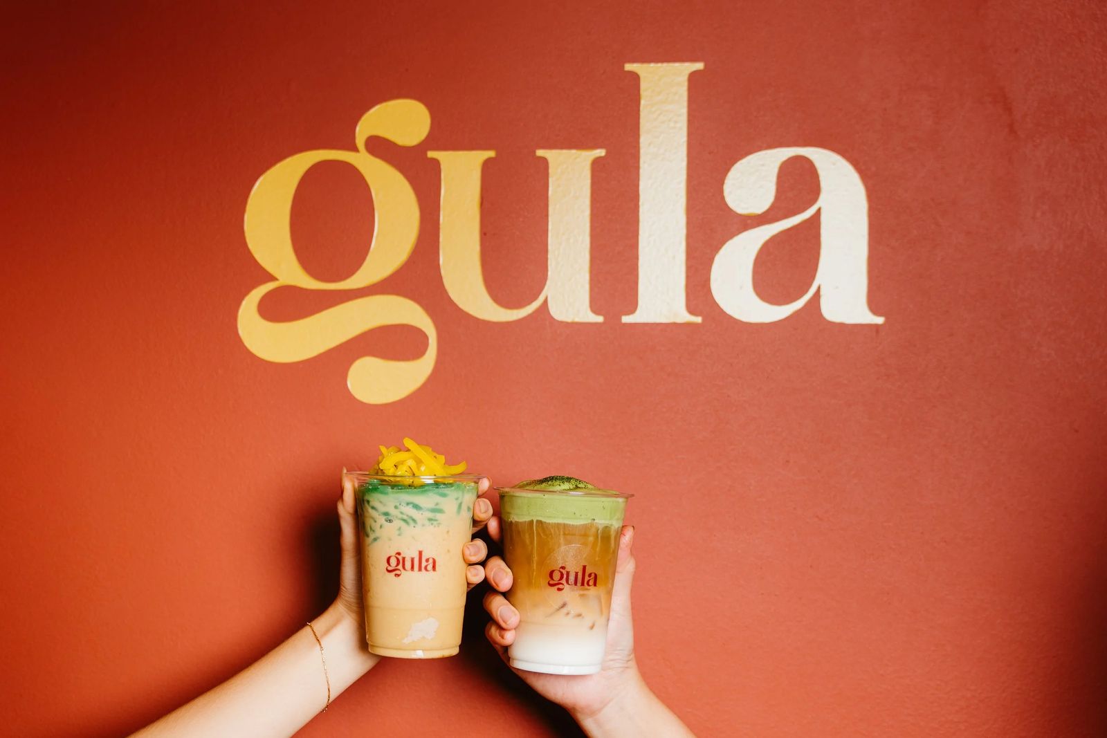 Gula drinks raised in front of the logo wall